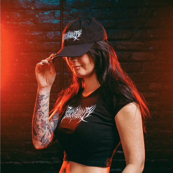 Person wearing a black cap and crop baby tee with visible branding against a dark background 