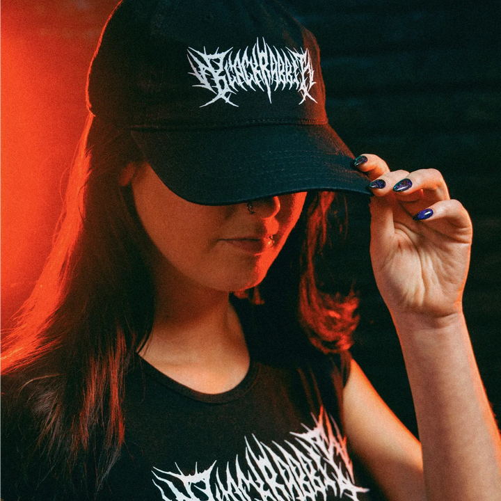 Person wearing a black cap and crop baby tee with white Black Rabbit design, set against a dark background. 