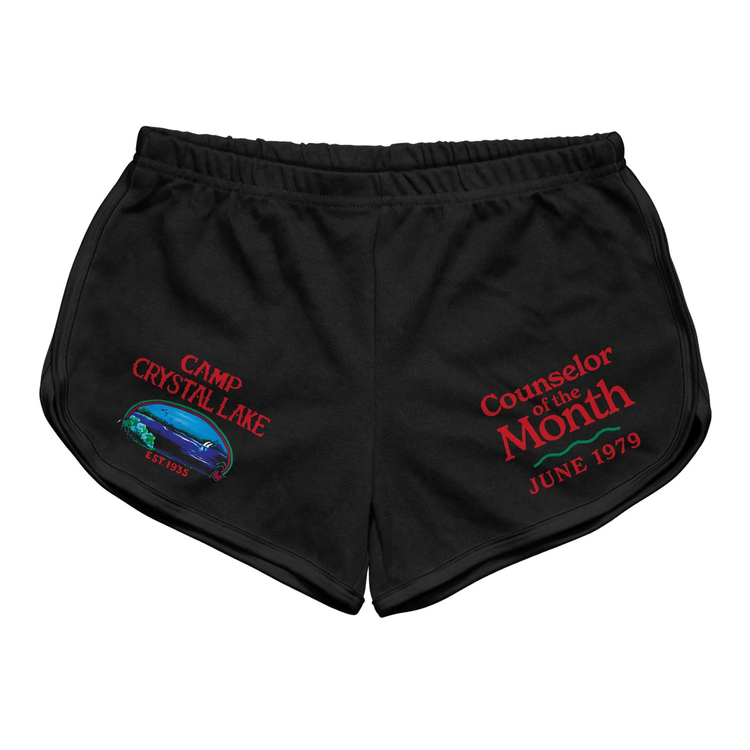 Black athletic shorts featuring embroidered red text and a colorful graphic of camp crystal lake with ’counselor of the month’ and ’june 1979.’