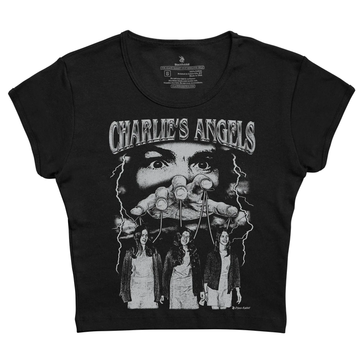 Black short-sleeved t-shirt featuring a white ’charlie’s angels’ graphic with lightning bolts and three women below a face holding marionette strings.