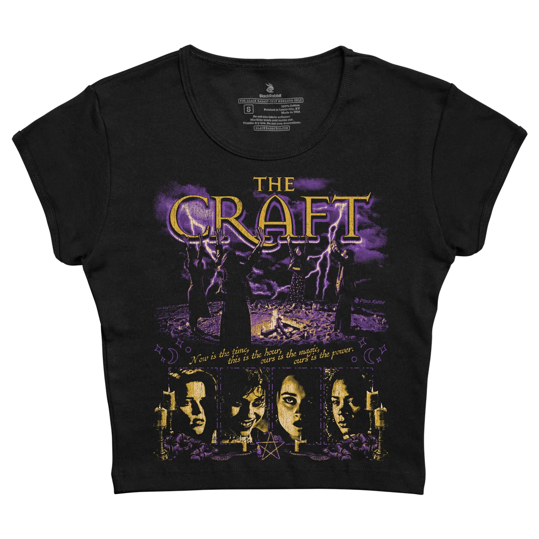 Black short-sleeved t-shirt featuring a purple and gold graphic of the movie ’the craft’ with silhouettes, lightning, candles, and faces beneath the title.