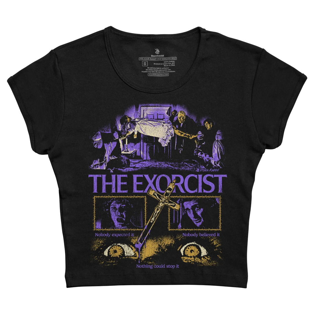 Black short-sleeved t-shirt featuring a purple and gold graphic of ’the exorcist’ movie poster with the taglines “nobody expected it” and “nothing could stop it.”