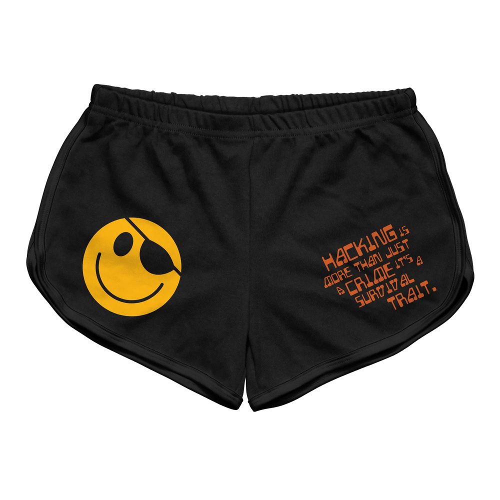 Black athletic shorts featuring a bold yellow smiley face with an eyepatch on the left leg and orange text reading ’hacking is more than just a craze, it’s a survival trait’ across the right thigh.