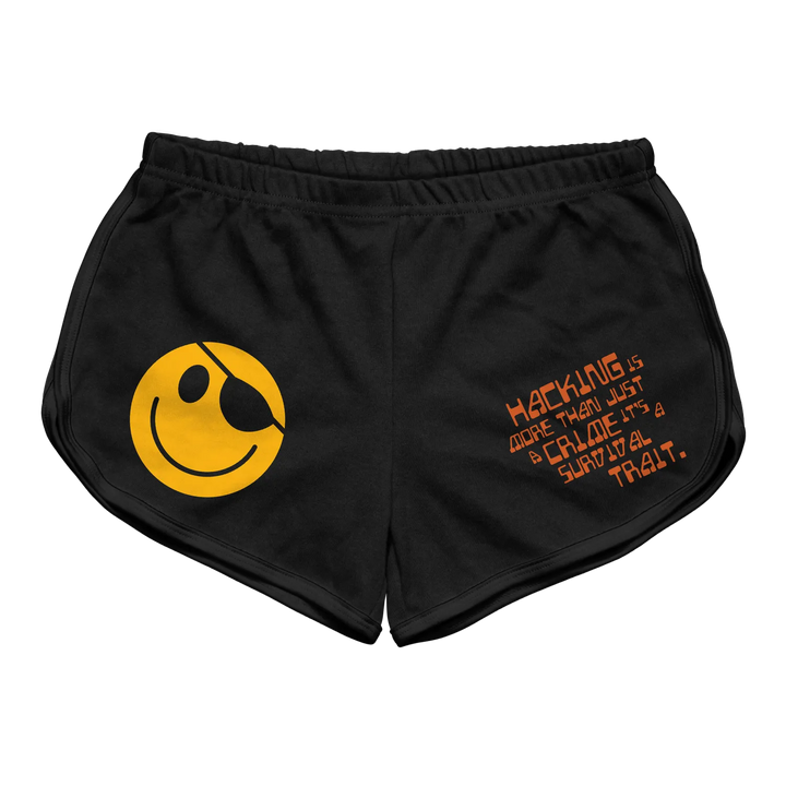 Black athletic shorts featuring a bold yellow smiley face with an eyepatch on the left leg and orange text reading ’hacking is more than just a craze, it’s a survival trait’ across the right thigh.
