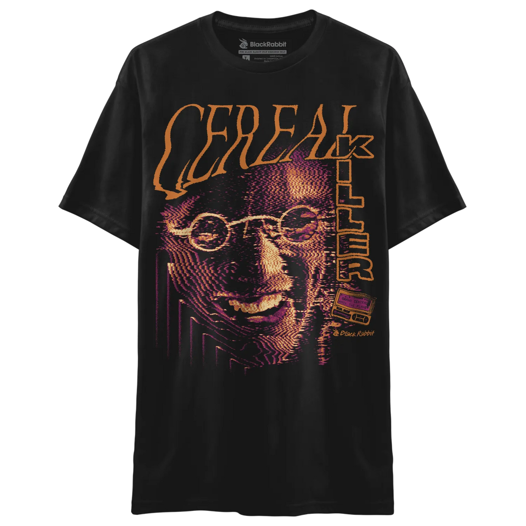 Black T-shirt with large Cereal Killer graphic featuring orange lettering, purple halftone face artwork, and retro horror-inspired design. 