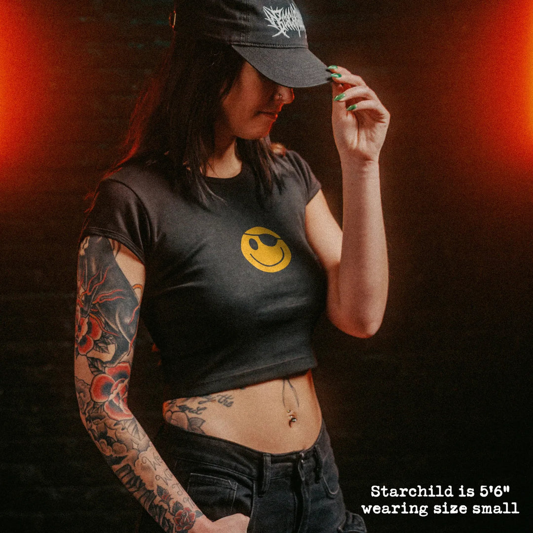 Female model wearing cropped baby tee with hackers pirate smiley graphic
