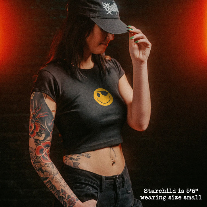 Female model wearing cropped baby tee with hackers pirate smiley graphic
