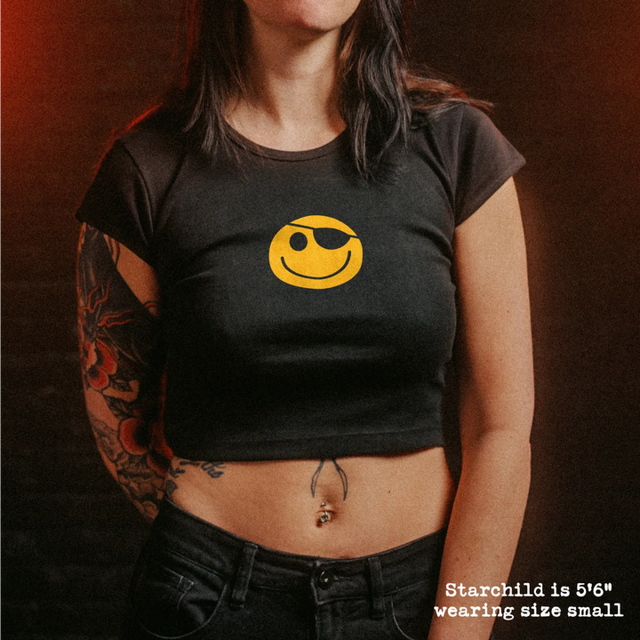 Female model wearing cropped baby tee with hackers pirate smiley graphic
