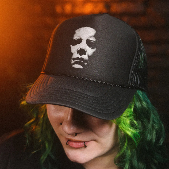 Female model with green hair wearing Black Rabbit's Black Foam Front Trucker Hat featuring white distressed Michael Myers mask graphic