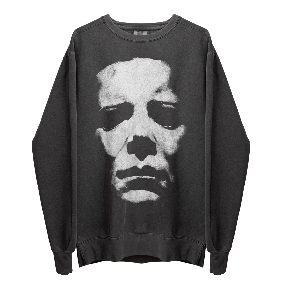 A dark gray crewneck sweatshirt with a large, distressed white graphic of a skull-like face on the front.