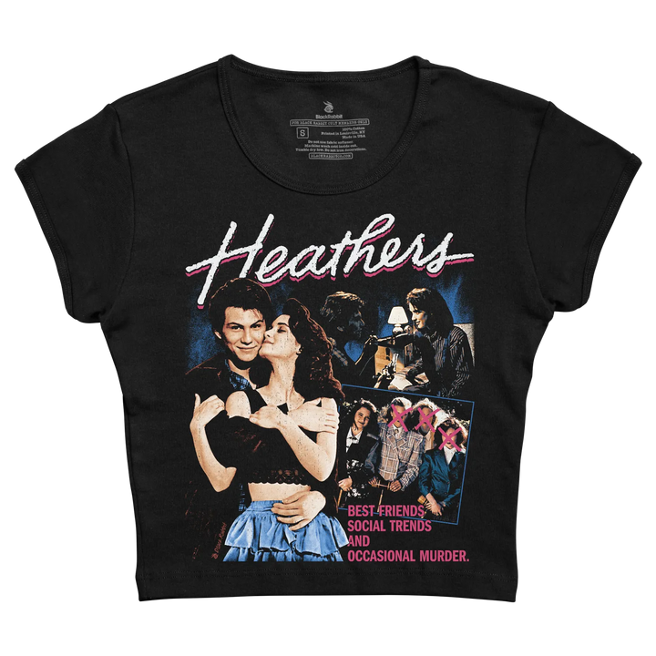 Black short-sleeved t-shirt featuring a vintage movie poster design for ’heathers’ with pink and white lettering, depicting characters in classic 1980s fashion.