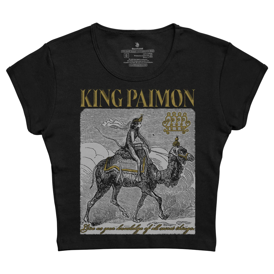 Black short-sleeved t-shirt featuring a detailed black-and-white illustration of king paimon riding a camel, accented with gold lettering and decorative elements.