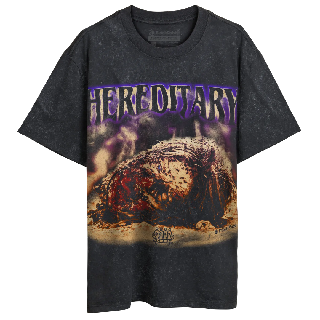 A dark gray, short-sleeved t-shirt with a distressed texture and a graphic print featuring purple ’HEREDITARY’ text and a gruesome, decaying head.