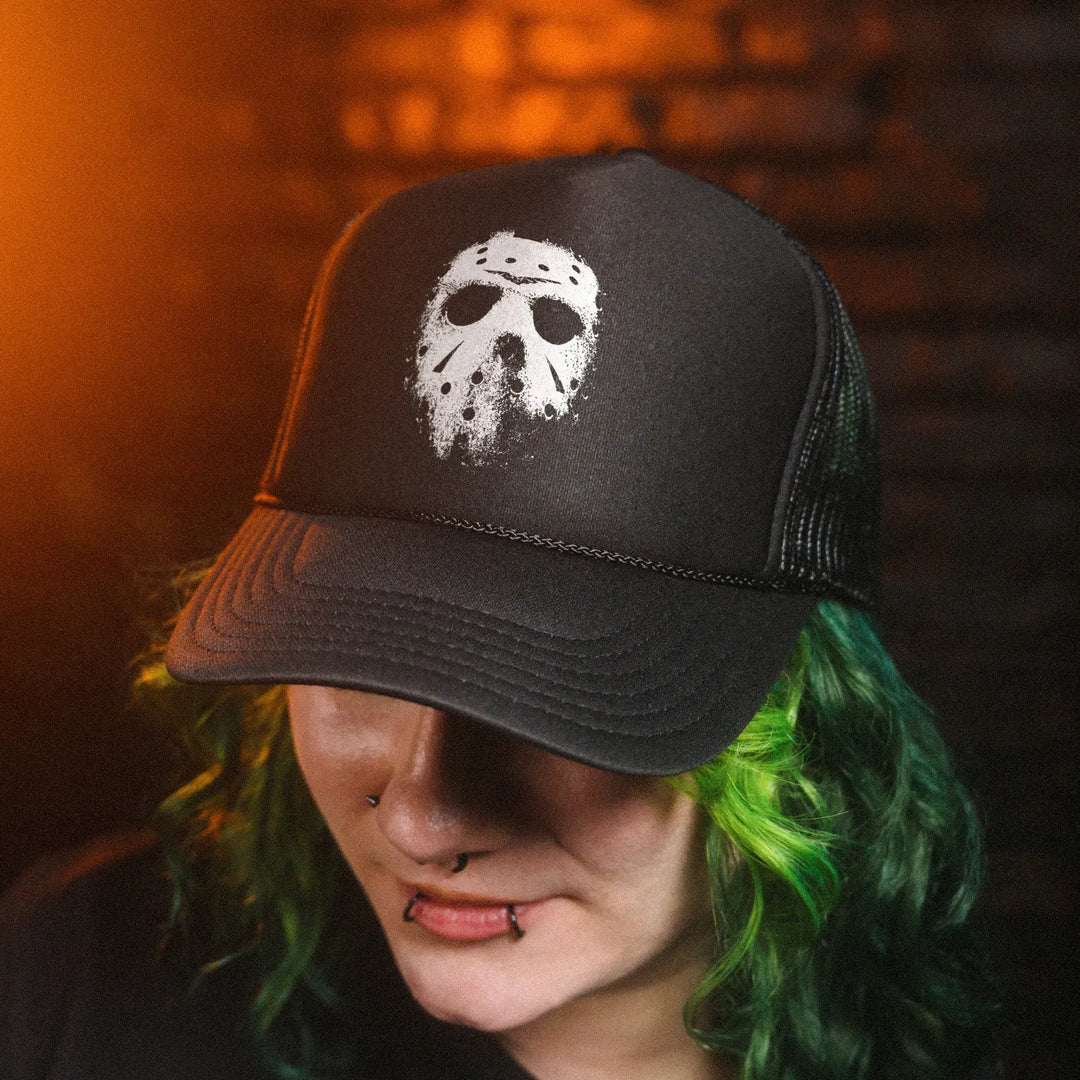 Female model with green hair wearing Black Rabbit's Black Foam Front Trucker Hat featuring white distressed hockey mask graphic