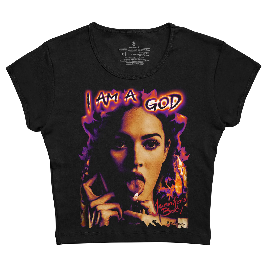 Black short-sleeved t-shirt featuring a vibrant graphic of a woman with fiery purple and orange flames surrounding her, the text ’i am a god’ above her head, and “jennifer’s body” written below. 