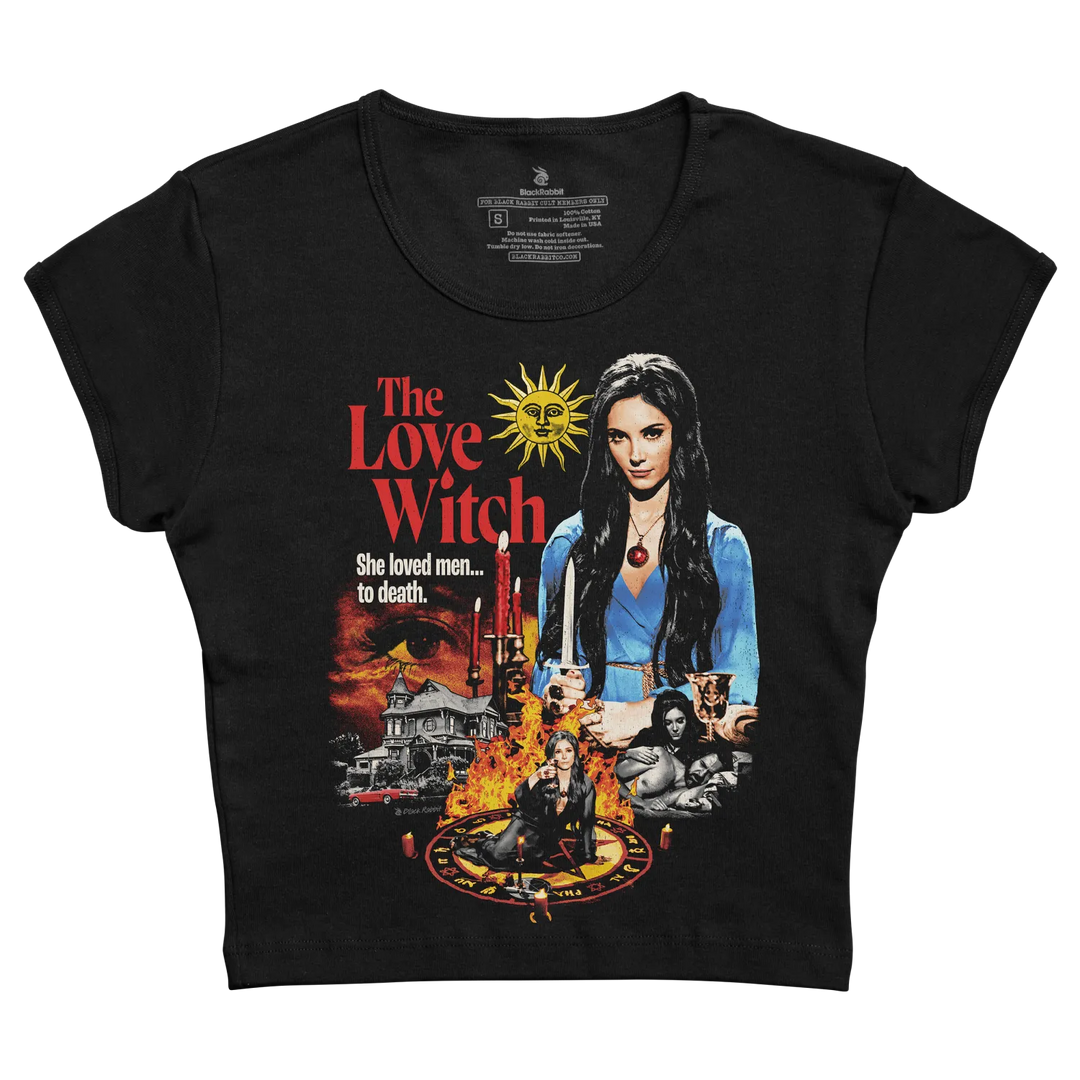 Black short-sleeved t-shirt featuring a vibrant graphic of ’the love witch’ movie poster with red and yellow text, an illustration of the main character in blue attire holding candles, surrounded by imagery including a house, flames, and occult symbols.