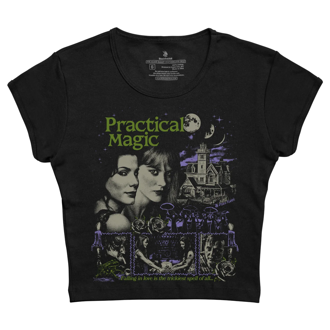 Black short-sleeved t-shirt featuring a graphic print of the movie ’practical magic’ with green and purple artwork depicting two women, a haunted house, and scenes from the film.