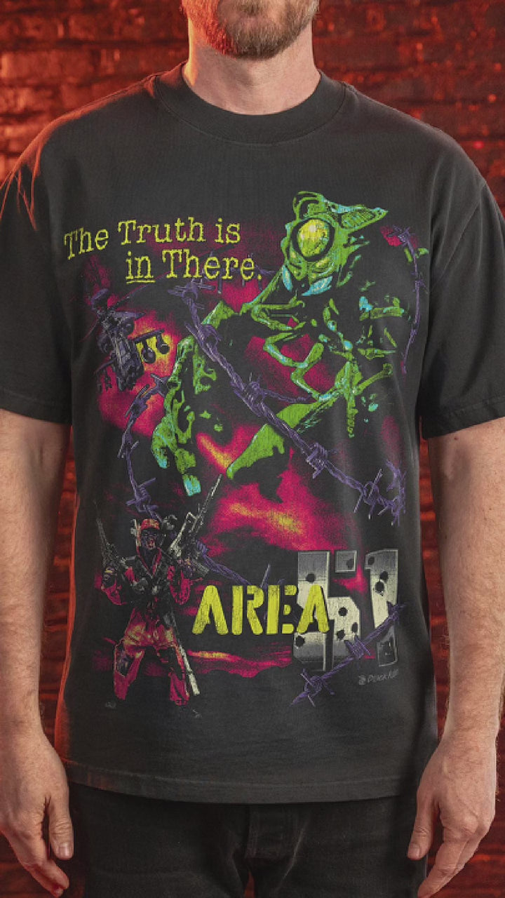 Male model wearing t-shirt with a vibrant, illustrative graphic featuring a green, insect-like creature 