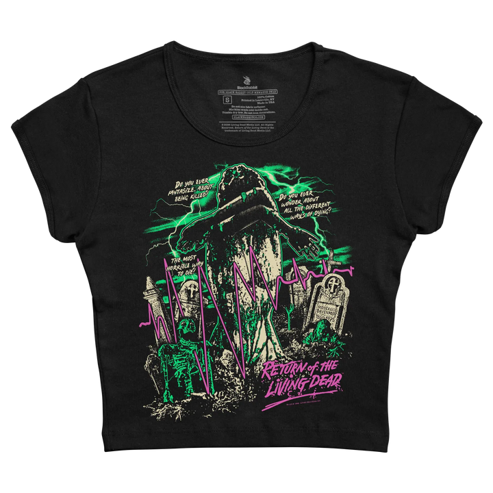 A black cropped women's baby tee featuring a horror-themed print of a zombie with tombstones, green lightning, and pink text reading 'Return of the Living Dead'.