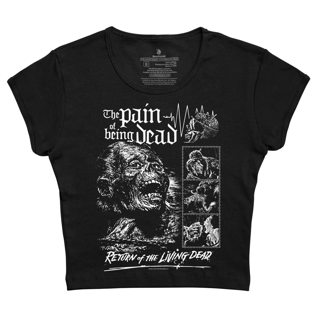 A black women's crop top baby tee featuring a white print of a zombie face and the text 'The pain of being dead' and 'Return of the Living Dead'.