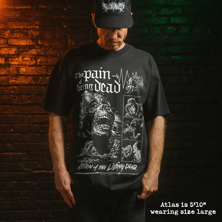 A man wearing a black graphic t-shirt brick wall lit with dramatic orange and green lighting. The t-shirt features a white graphic print.