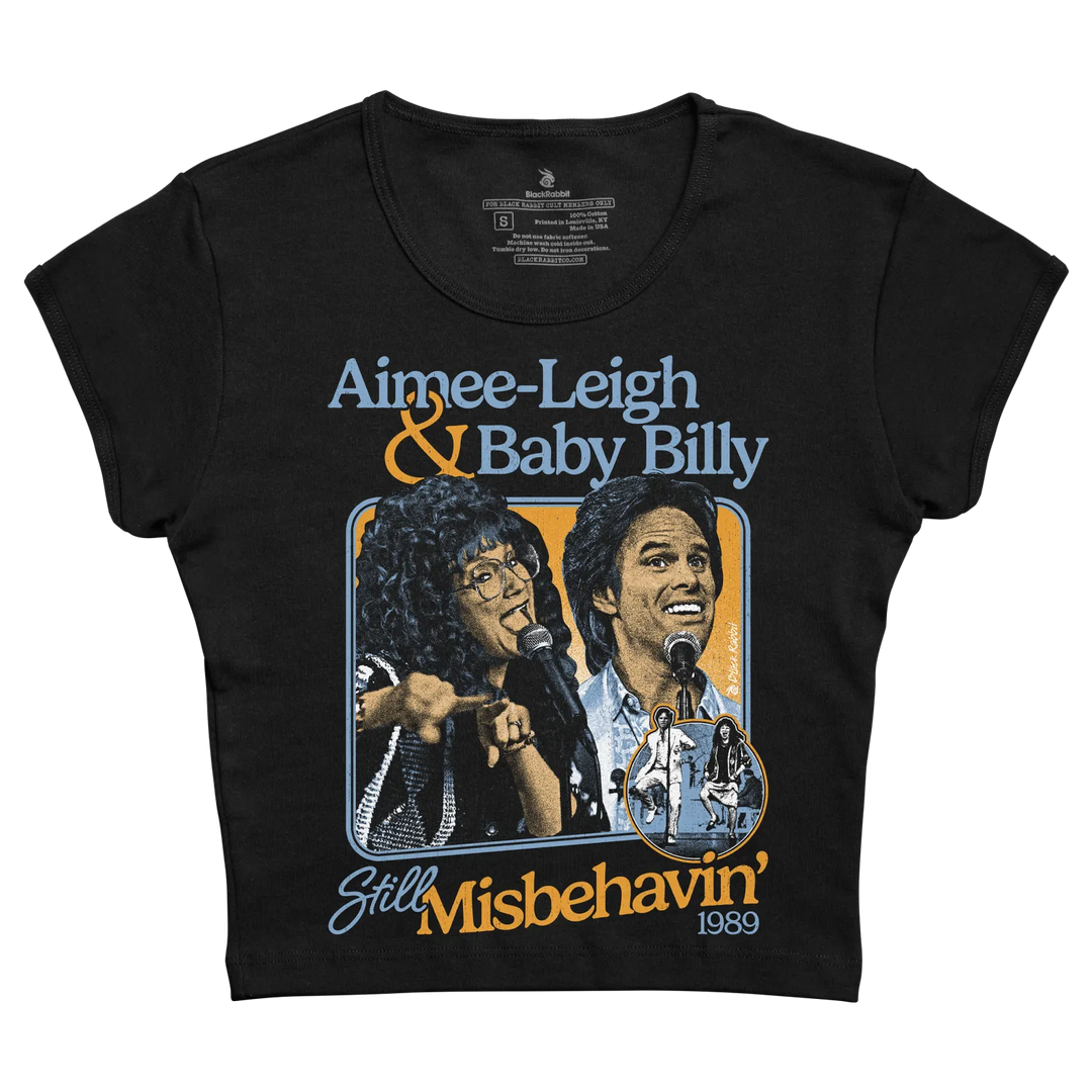 Black short-sleeved t-shirt featuring a vintage graphic of aimee- leigh and baby billy from the 1989 musical ’still misbehavin’’ with stylized blue, orange, and white lettering.
