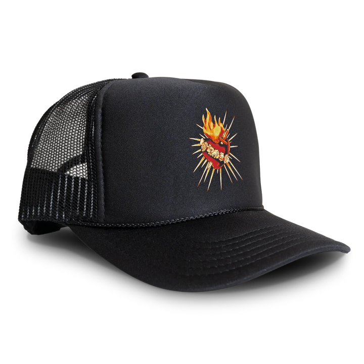 A black trucker hat with a black mesh back, featuring a graphic of a red heart with flames and gold teeth on the front panel. 