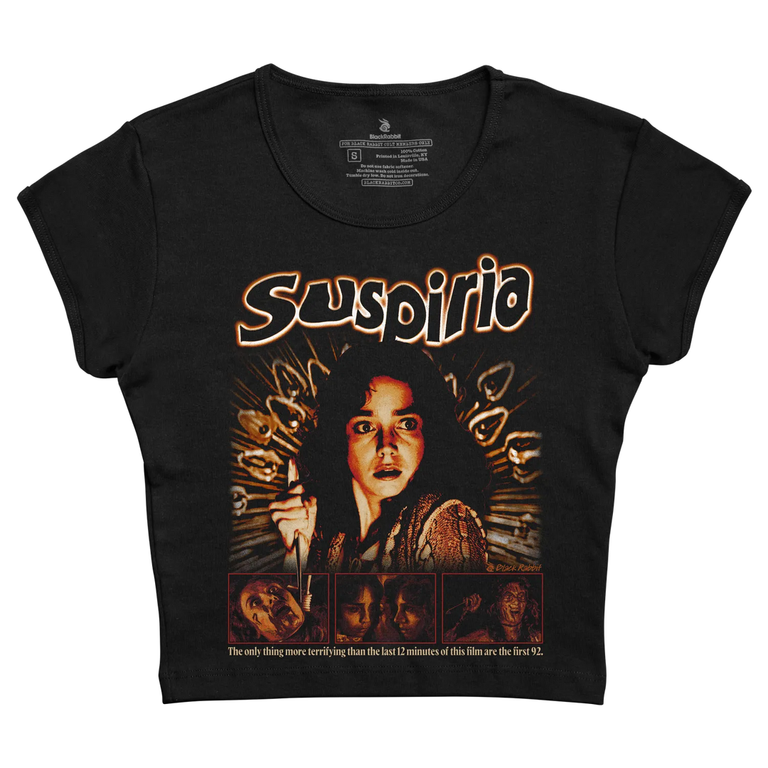 Black short-sleeved t-shirt featuring a graphic print of the movie ’suspiria’ with orange and brown tones, depicting a woman holding a knife surrounded by ghostly faces.