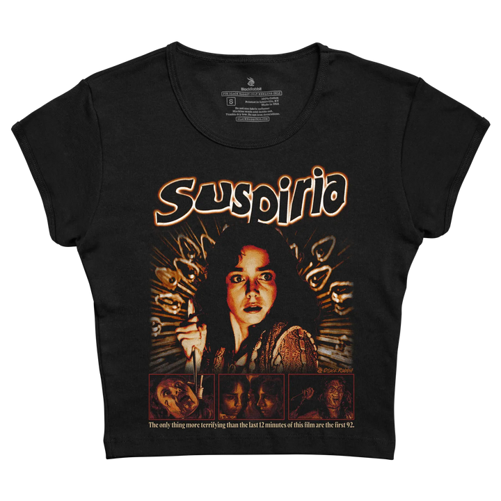 Black short-sleeved t-shirt featuring a graphic print of the movie ’suspiria’ with orange and brown tones, depicting a woman holding a knife surrounded by ghostly faces.